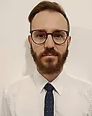 Homem com óculos e gravata, vestindo camisa branca, em fundo neutro. Imagem para representar Projetos Acústicos, Consultoria Acústica e Engenharia Acústica.